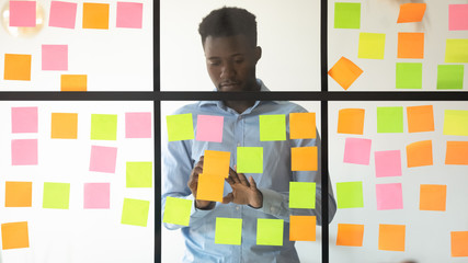Concentrated african american young manager adding tasks on glass wall.
