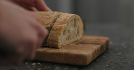 man slicing ciabatta with bread knife on olive board