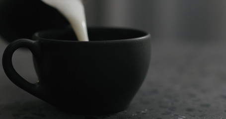 pouring steamed milk into cappuccino in black cup on terrazzo countertop