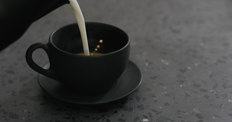 pouring steamed milk into cappuccino in black cup on terrazzo countertop