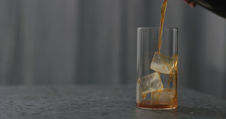 pour coffee over ice cubes in glass to make iced coffee on terrazzo countertop