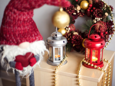Vintage Christmas Lanterns Red and gray with burning Candles and gray dwarf in red hat with red heart in hands. Cozy christmas decorations with golden beads and balls. Christmas tree on background.