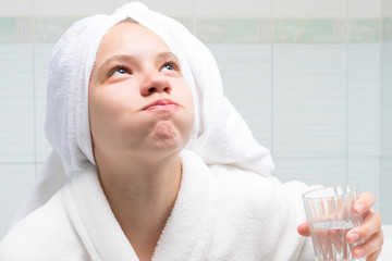 baby girl, in a white robe and towel on her head, in the bathroom, holding a glass of water and...