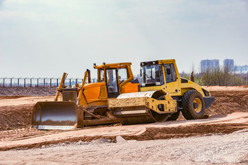 Obraz premium Road roller and bulldozer stand on sand surface during the new road construction process.