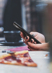 woman hand using mobile phone in cafe with a piece of pizza in plate on table