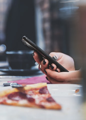 Fototapeta premium woman hand using mobile phone in cafe with a piece of pizza in plate on table