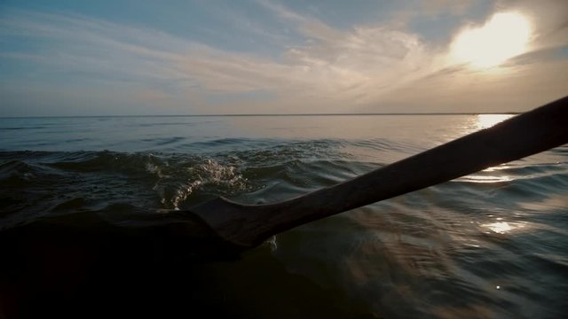 Old wooden oar pull lake water and make splashes. Rowing boat ride on lake. Blue sunset sky and clouds reflected in the water. Drops of water dripping from the paddles, patterns on water.