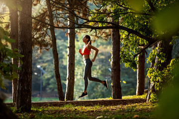 Side view of slim attractive caucasian brunette in sportswear and with ponytail running on trail in woods. Morning fitness in nature.