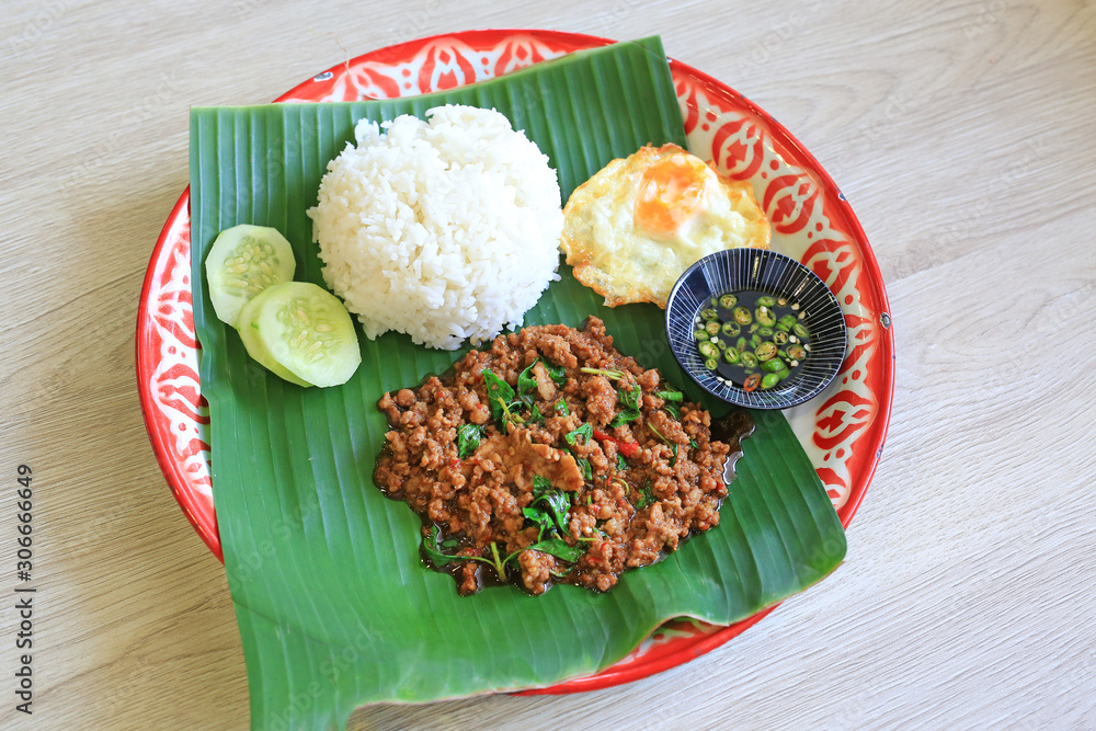 Poster stir-fried minced pork with basil leaves served with rice and fried egg on banana leaf on zinc tray 