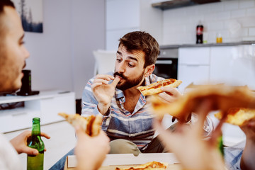Group of friends sitting on the floor in living room, drinking beer and eating pizza. House party.