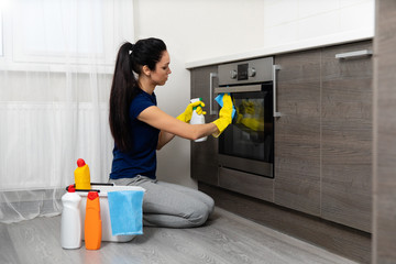 people, housework and housekeeping concept - close up of woman hand in protective glove with rag cleaning cooker at home kitchen