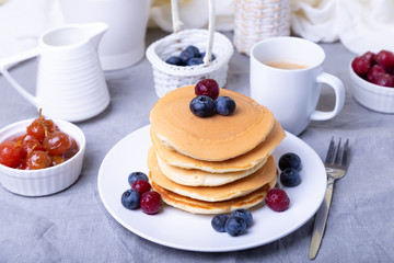 Pancakes with blueberries, cherries and mini apple jam. A cup of coffee and gravy boat in the background. Traditional american pancakes. Close-up.