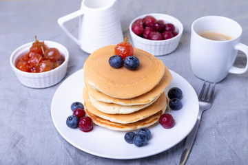 Pancakes with blueberries, cherries and mini apple jam. A cup of coffee and gravy boat in the background. Traditional american pancakes. Close-up.