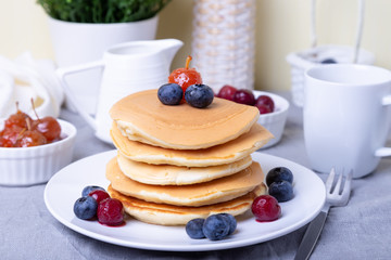 Pancakes with blueberries, cherries and mini apple jam. A cup of coffee and gravy boat in the background. Traditional american pancakes. Close-up.