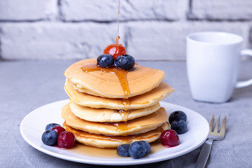 Pancakes with maple syrup, blueberries, cherries and a mini apple. Maple syrup pours on pancakes. A...