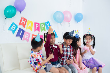 Adorable Asian schoolkids group with beautiful dresses enjoy the birthday party at home with many gift boxes , juices, and bakery