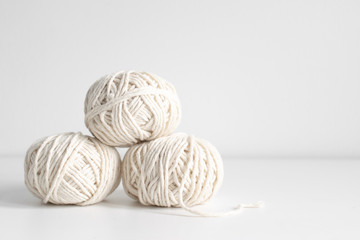 Balls of white yarn on a white wall background. Threads of wool boho image. Space for text. Good...