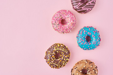 Pattern with different types of colorful donats decorated sprinkles and icing on a pastel pink background, top view flat lay