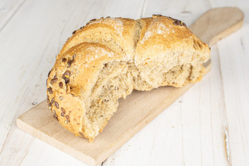 One whole sesame kaiser roll on wooden cutting board on white wood