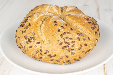 One whole sesame kaiser roll on white ceramic plate on white wood