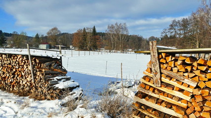 Winterlandschaft in Bayern, Brennholzstapel im Schnee, Dorfidylle im Winter