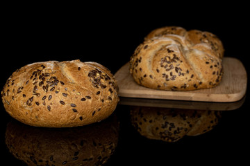 Group of two whole baked sesame kaiser roll on bamboo cutting board isolated on black glass