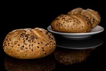 Group of three whole sesame kaiser roll on white ceramic plate isolated on black glass
