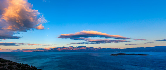 Cretan seascape at sunset with mountains, moon and clouds. Crete, Greece.