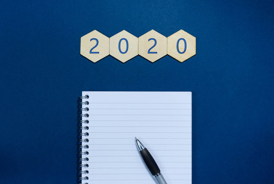 2020 written on wooden hexagons  with notepad and pen in a conceptual image of the coming new year and new year resolutions. Over blue background with copy space.
