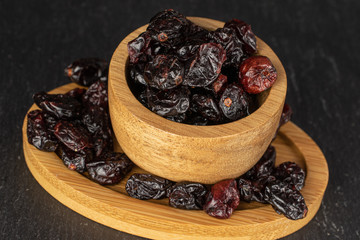 Lot of whole dried cowberry................ in bamboo bowl on round bamboo coaster on grey stone