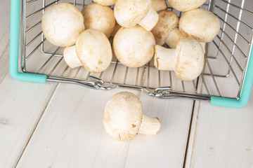 Lot of whole fresh white champignon on shopping basket on white wood