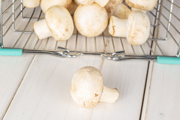 Lot of whole fresh white champignon on shopping basket on white wood