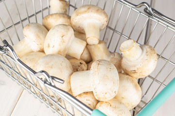 Lot of whole fresh white champignon on shopping basket on white wood