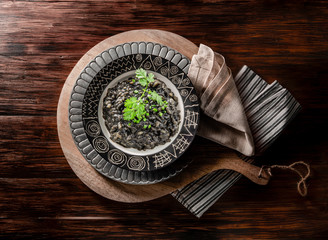 arroz negro con perejil sobre plato de diseño sobre mesa de madera, vista cenital. Black rice with parsley on designer plate on wooden table, overhead view.