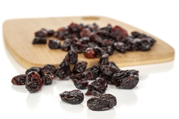Lot of whole disordered dried cowberry................ on bamboo cutting board isolated on white background