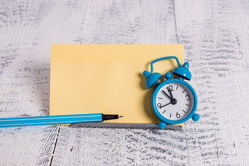 Mini blue alarm clock stand tilted above buffer wire in front of notepaper