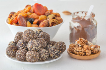 Natural healthy raw energy bites, chocolate paste and mix of dried fruits with nuts on a white table. Close-up