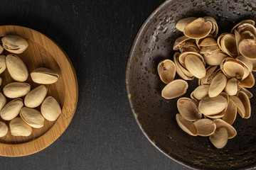 Lot of whole salted pistachio on round bamboo coaster in glazed bowl flatlay on grey stone