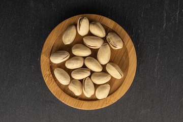 Lot of whole salted pistachio on round bamboo coaster flatlay on grey stone