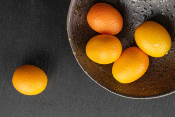 Group of five whole tasty orange kumquat in glazed bowl flatlay on grey stone