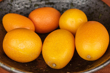 Group of six whole tasty orange kumquat in glazed bowl on cognac leather