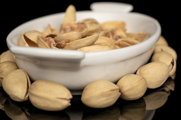 Lot of whole salted pistachio in small white ceramic bowl isolated on black glass