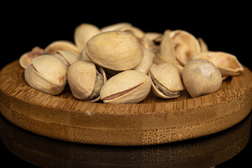 Lot of whole salted pistachio on round bamboo coaster isolated on black glass