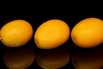 Group of three whole tasty orange kumquat isolated on black glass