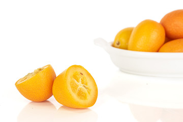 Group of four whole two halves of tasty orange kumquat in small white ceramic bowl isolated on white background