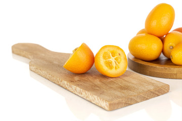 Group of six whole two halves of tasty orange kumquat on wooden cutting board on round bamboo coaster isolated on white background