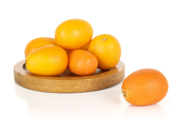 Group of six whole tasty orange kumquat on round bamboo coaster isolated on white background