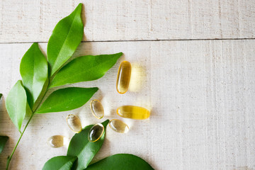 Top view of natural vitamins supplement on white wood background with green leaves.