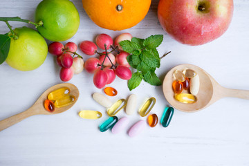 Multivitamin supplements from fruit on white wooden background
