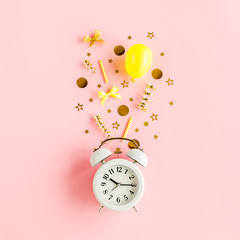 Alarm clock and gold confetti, balloons, streamers and decoration on a pink background. Colorful...